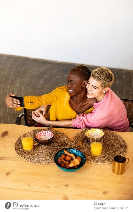 Beautiful young bestfriend females taking selfie using a smart phone and smiling while having a breakfast at home friendship domestic life together sitting