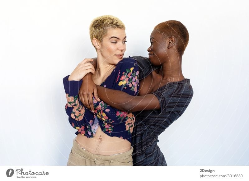 Photo of joyful ladies embrace and enjoy togetherness, being of different of races, dressed in casual jumpers, isolated over white background. bestfriend