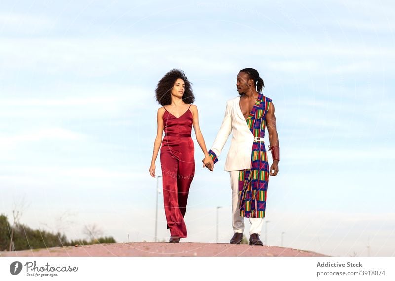 Stylish black couple on the road against blue sky fashion trendy outfit model hug together apparel style ethnic holding hands walk african american fancy