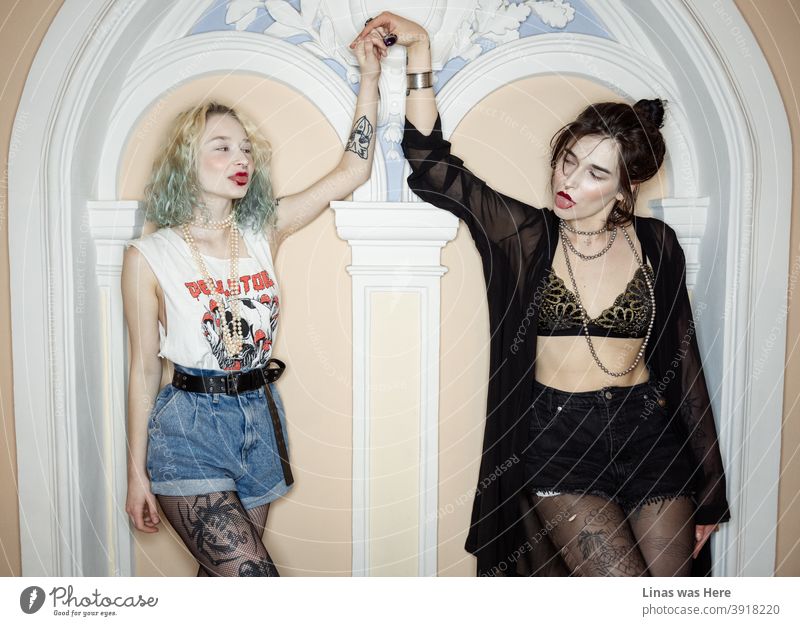 Young blood and positive energy. Two wild girls with tattoos are holding hands inside a fancy mansion with a classy interior. Girls just want to have fun!