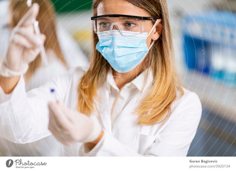 Woman doctor wearing protective  face mask in lab hold needle syringe and medicine vial vaccine bottle medical drug laboratory science care vaccination hospital