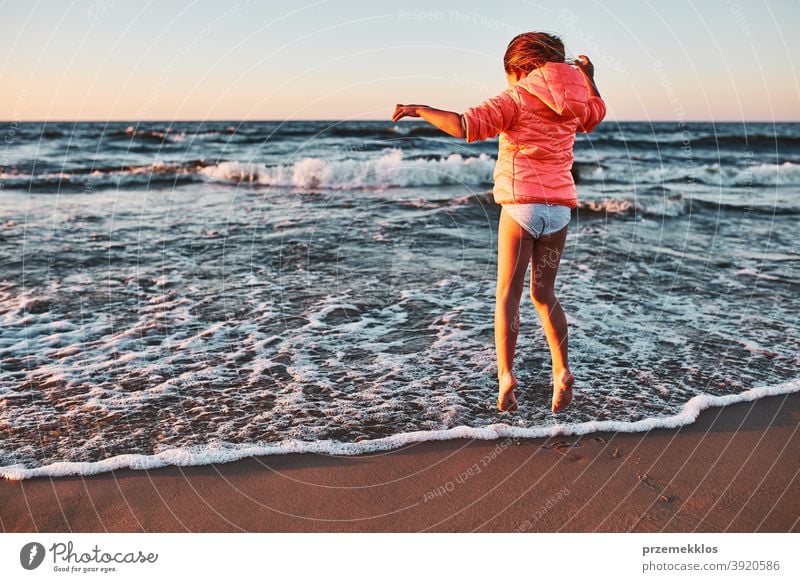 Playful little girl jumping over sea waves on a sand beach at sunset excited free enjoy positive emotion carefree nature outdoors travel happiness happy summer