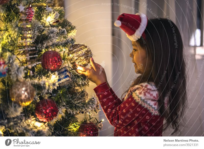 Little girl dressed in a Christmas sweater and a Christmas hat, hanging the Christmas balls on the tree. nice open beautiful magic background portrait woman box