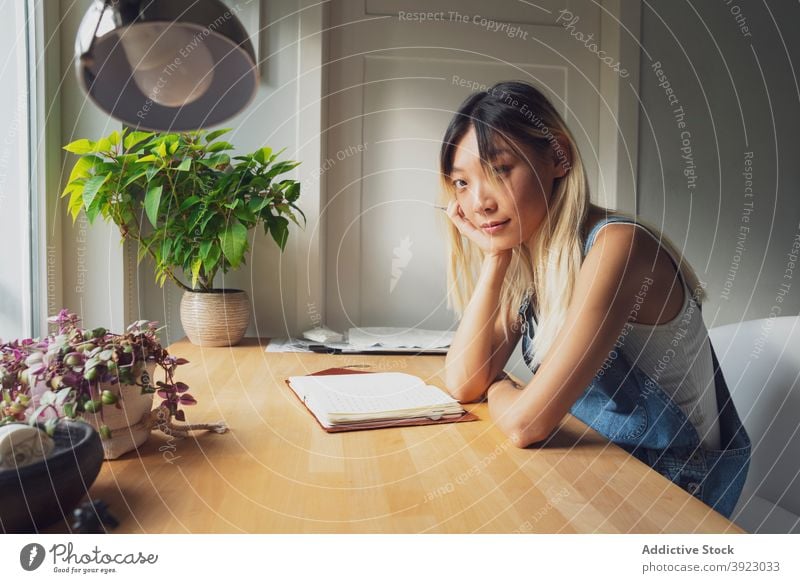 Ethnic woman taking notes in notebook at home take note thoughtful diary lean on hand think notepad table female asian ethnic pensive relax casual content style