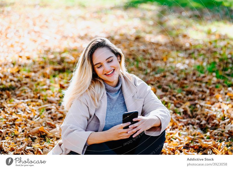 Positive woman sending message on mobile phone in park speak smartphone enjoy conversation cheerful autumn female gadget content device cellphone happy optimist