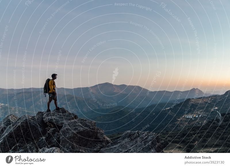 Traveling man standing on rocky summit at sunset traveler mountain freedom lonely explorer rough adventure backpack top nature male wanderlust hike highland