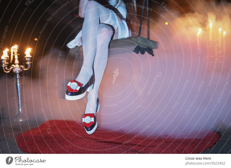 Fashionable girl with avant-garde shoes swinging under the bridge. Smoke with chandeliers creates a mystic atmosphere. This is not a typical fashion photoshoot.