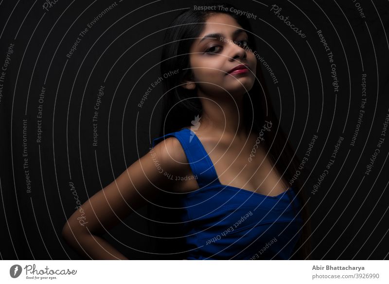 Fashion portrait of an young and attractive Indian Bengali brunette girl with blue western dress in front of a black studio background. Indian fashion portrait and lifestyle.