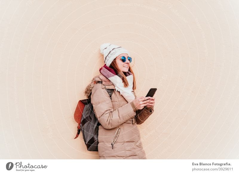 woman using mobile phone over yellow wall background. Technology and winter concept outdoors city technology lifestyles sunglasses modern app video working call