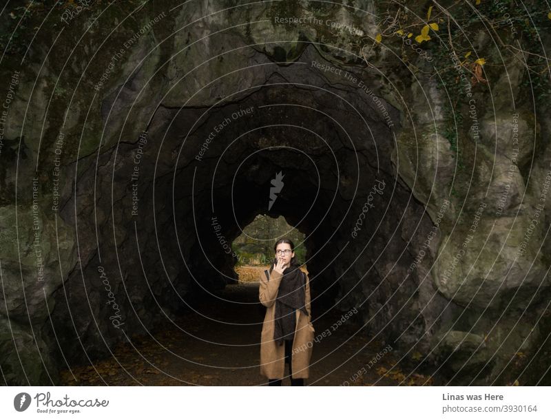 It’s autumn in Ghent, Belgium. The brunette girl is dressed in a fashionable brown coat and a long black scarf is a must during this dreadful weather. She’s smoking a cigarette next to a cave.