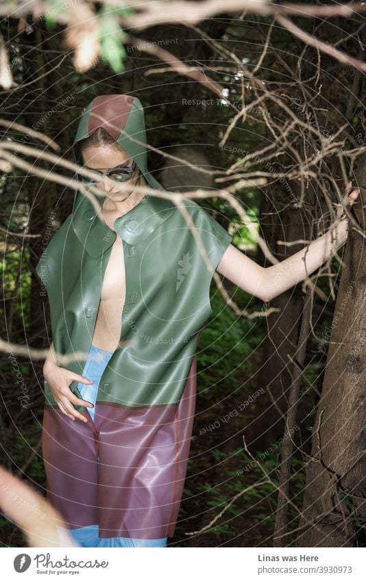 A gorgeous fashion model is posing in dark woods. She is dressed in a colourful raincoat. A fashionable girl with sexy curves and sunglasses is lost in this moody forest.