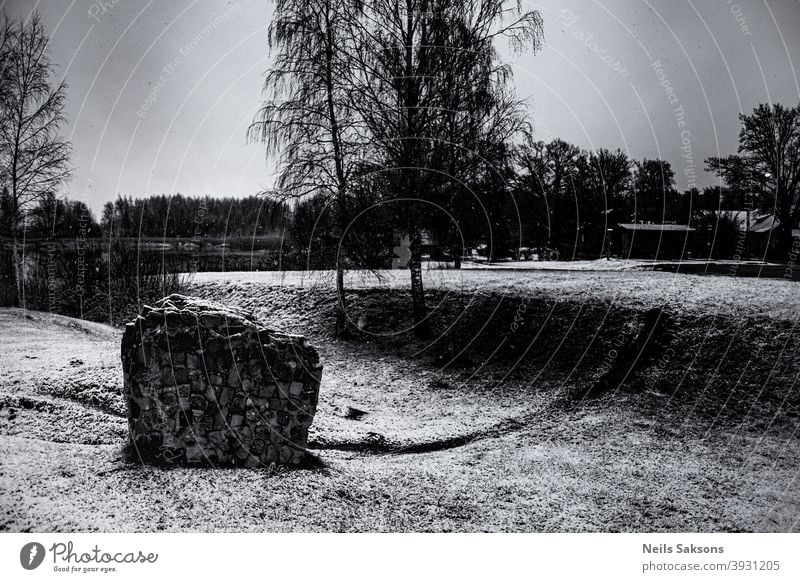 fragment of brick wall in park. landscape with birches, pond and sculptural element. snowy winter day in Latvia. piece lanscape trees trail pathway harsh