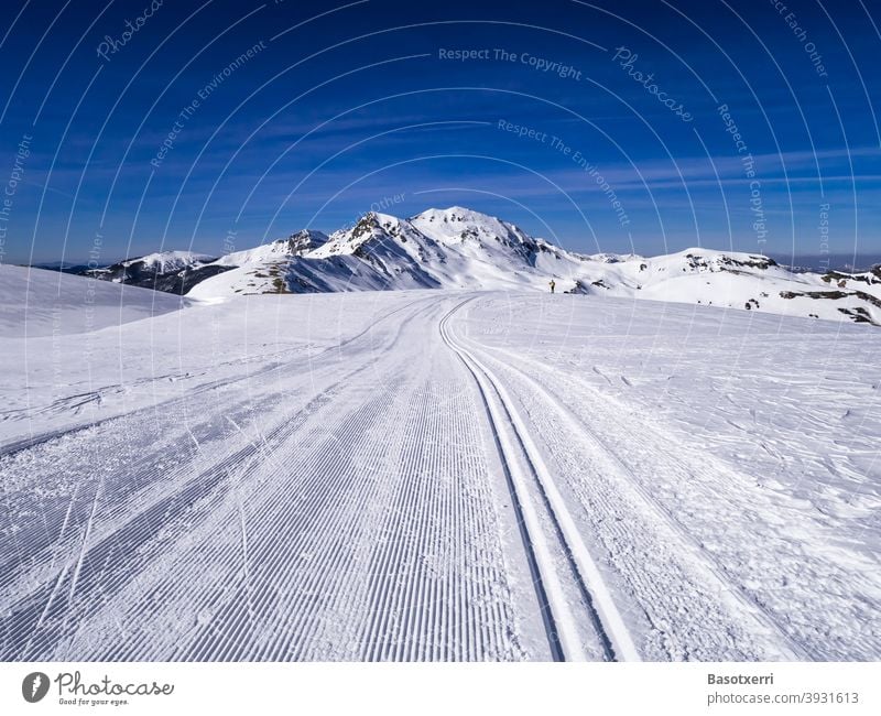 Traced cross-country skiing track in the mountains. Small person (cross-country skier) in the background. Isaba/Belagua, Navarra in the Spanish Pyrenees.