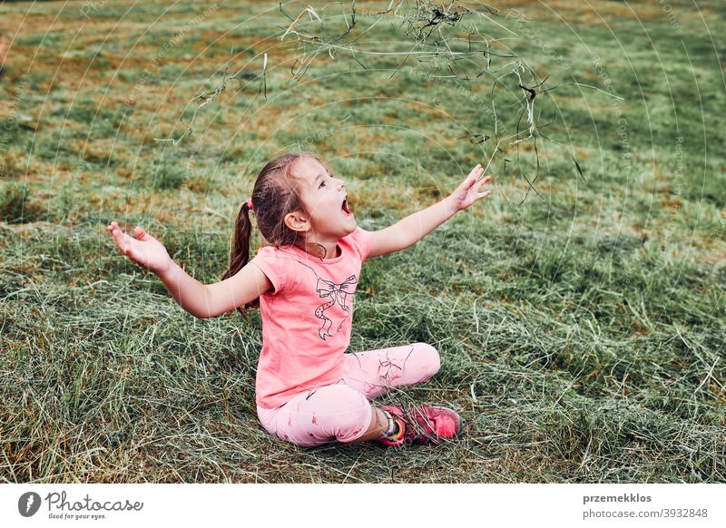 Little girl playing with grass enjoying summer day playing in the field during vacation trip happy excitement enjoyment leisure emotion positive lying lifestyle