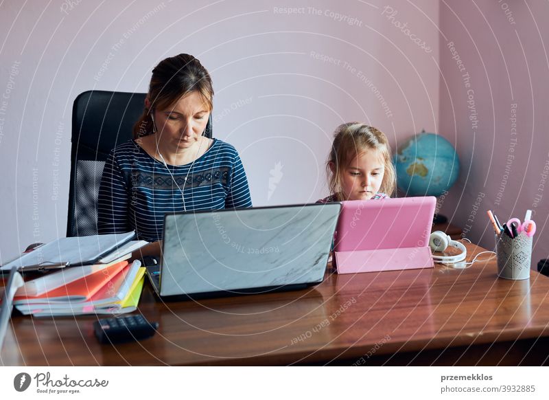 Woman mother working doing her job remotely during video chat call stream online course webinar on laptop from home while her daughter watching video on tablet