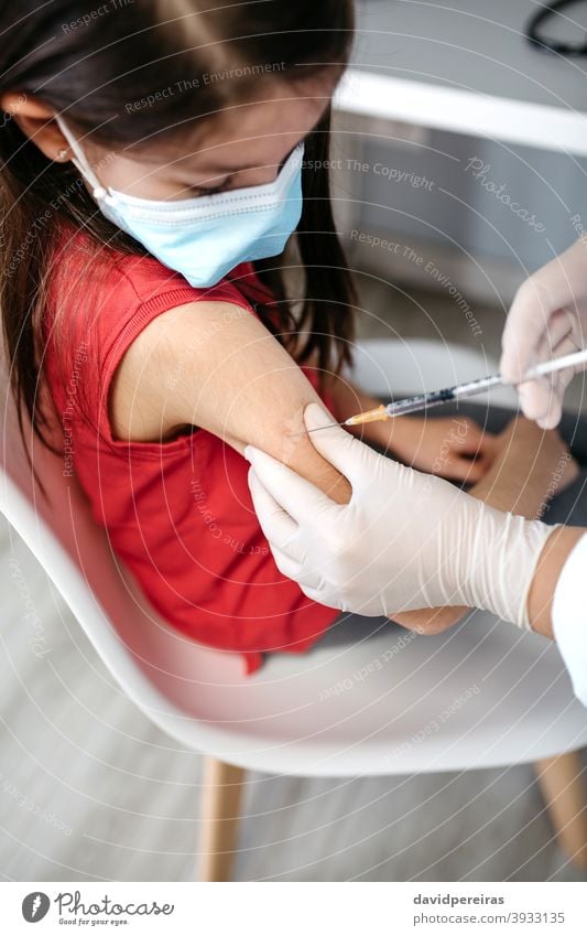 Girl receiving coronavirus vaccine at doctor's office injecting covid-19 little girl syringe top view hand immunization injection vaccination kid child