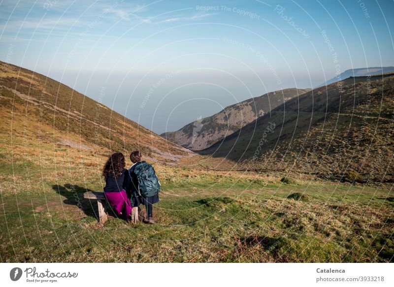 Young couple sitting on a bench enjoying the sea view during a hiking break Nature Landscape Ocean Hill cliffs Plant Grass bushes Wooden bench Sit Observe