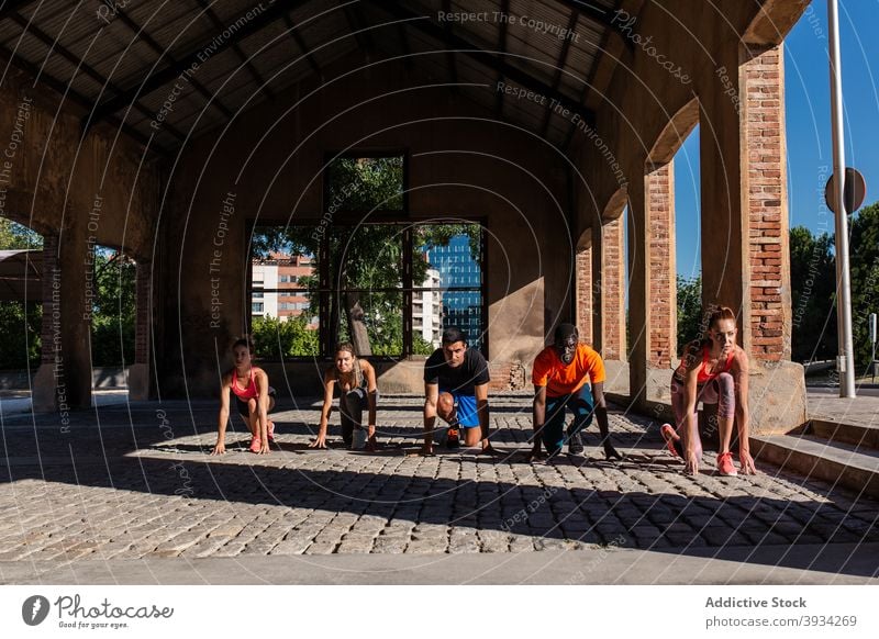 Company of runners in crouch start pose during training sportspeople challenge ready position group athlete professional city multiethnic multiracial diverse