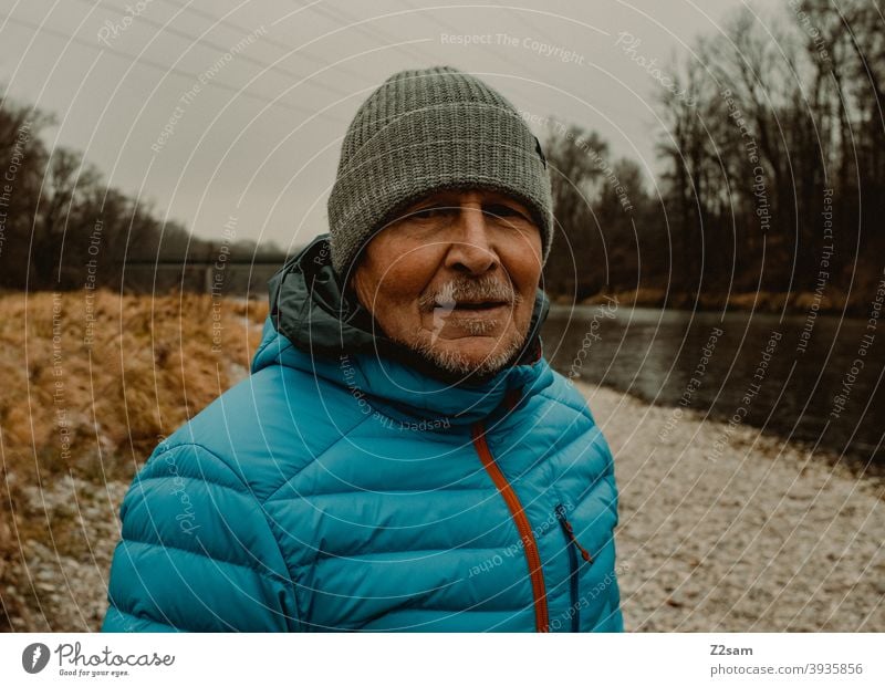 Portrait eines sportlichen Rentners in der Natur spazieren natur outtdoor rentner alter mann portrait mütze winter kälte landschaft wald sträucher isar freizeit