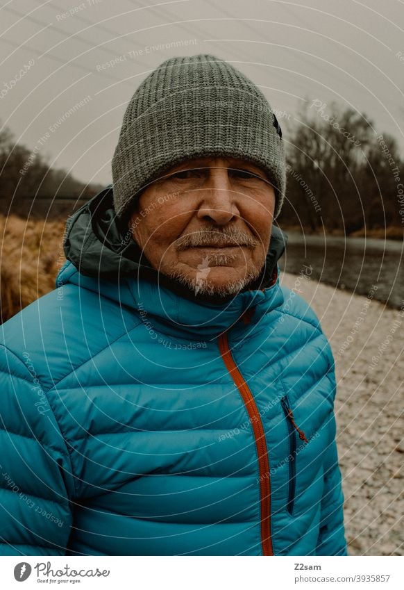 Portrait eines sportlichen Rentners in der Natur spazieren natur outtdoor rentner alter mann portrait mütze winter kälte landschaft wald sträucher isar freizeit