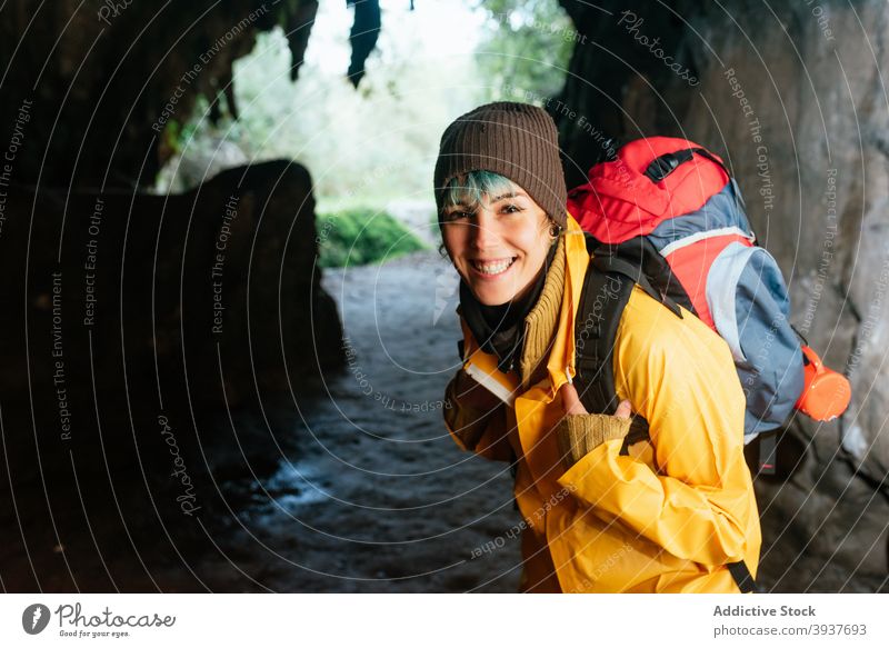 Delighted female explorer with backpack looking at camera traveler woman cheerful passage arch rocky outerwear autumn vacation cobijero beach asturias spain