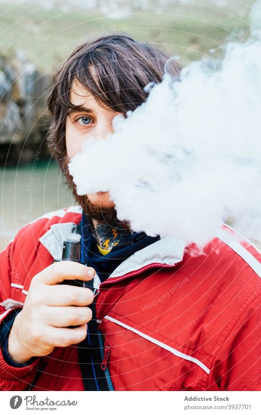 Man smoking e cigarette and looking at camera man smoke vape electronic fume smoker autumn outerwear beach male cobijero beach asturias spain exhale rest