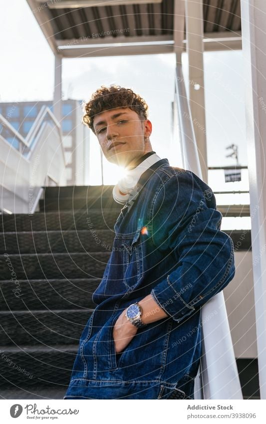 Young man with headphones standing on stairs listen city wireless young male relax curly hair audio joy positive rest style urban street handsome carefree