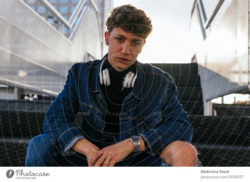 Young man with headphones sitting on stairs listen city wireless young male relax curly hair audio joy optimist positive rest style urban street handsome