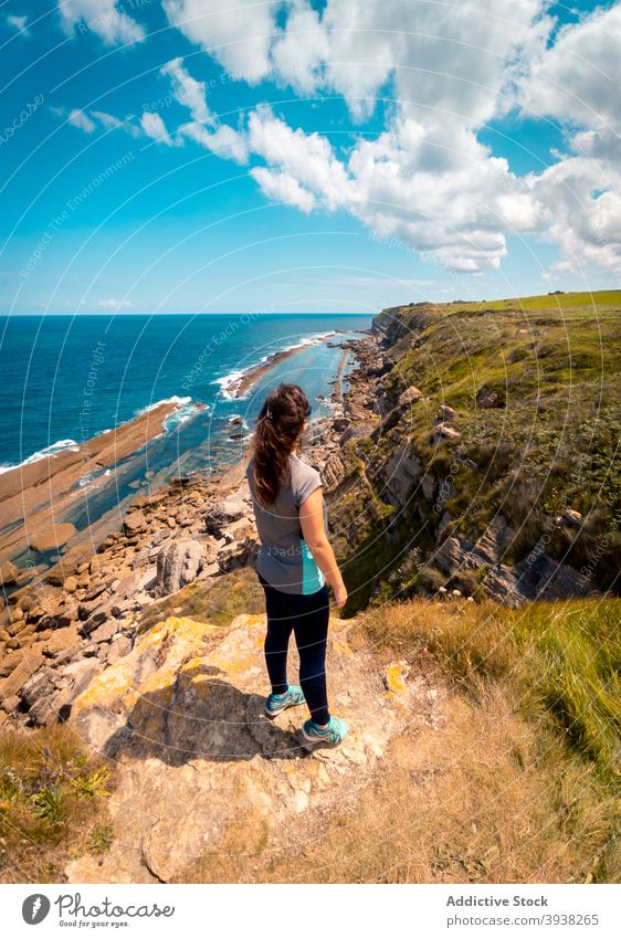 Anonymous woman walking towards wavy sea surrounded by rocky cliffs in sunny day coast road traveler sunset sky seascape sundown ocean female young explore