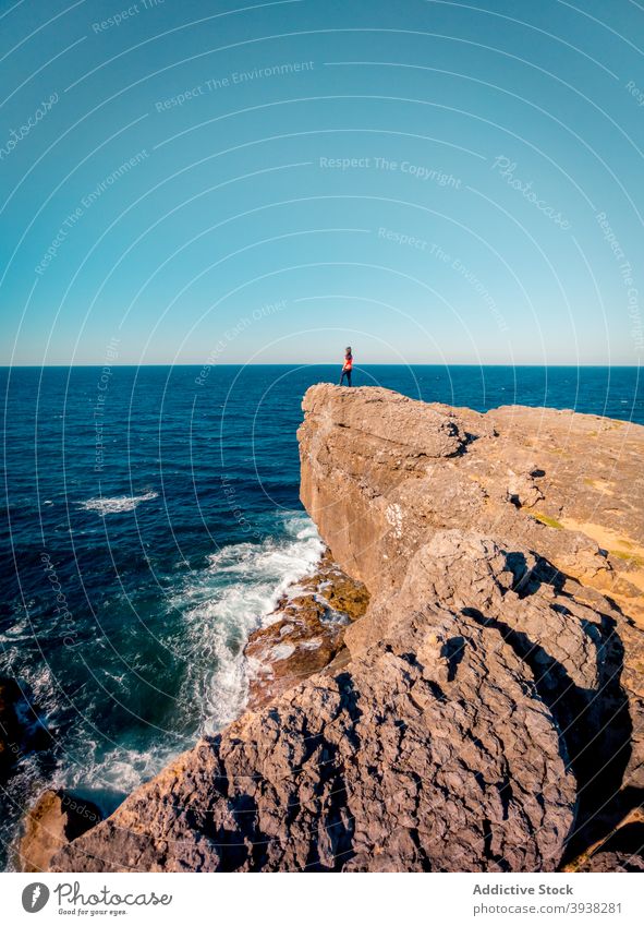 Anonymous woman standing on rocky cliff and enjoying amazing seascape on sunny day admire wanderlust hiker vacation travel nature landscape seafront female