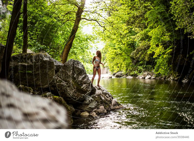 Gorgeous young tanned lady in swimwear relaxing on rocky cliff near lake in forest woman rainforest traveler vacation allure gorgeous confident nature holiday