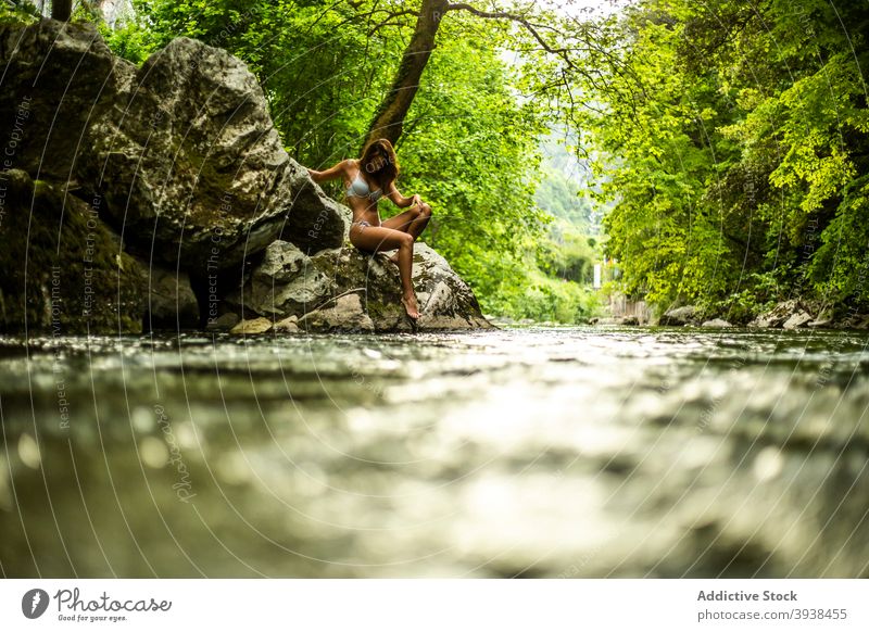 Gorgeous young tanned lady in swimwear relaxing on rocky cliff near lake in forest woman rainforest traveler vacation allure gorgeous confident nature holiday