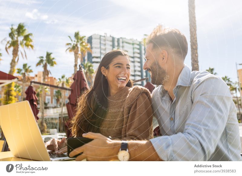 Young ethnic man kissing cheek of smiling girlfriend working remotely on netbook in cafeteria couple hug love romantic laptop together distance affection