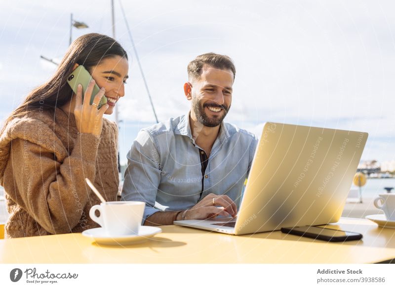 Young ethnic man kissing cheek of smiling girlfriend working remotely on netbook in cafeteria couple hug love romantic laptop together distance affection