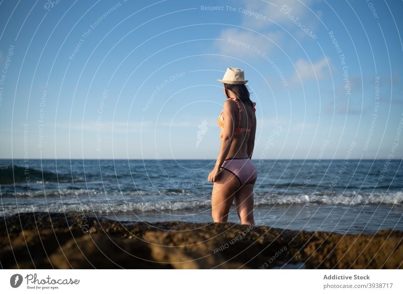 Unrecognizable female traveler enjoying sunny day on rocky seashore woman sunbath beach relax holiday resort ocean coast young swimwear straw hat suntan