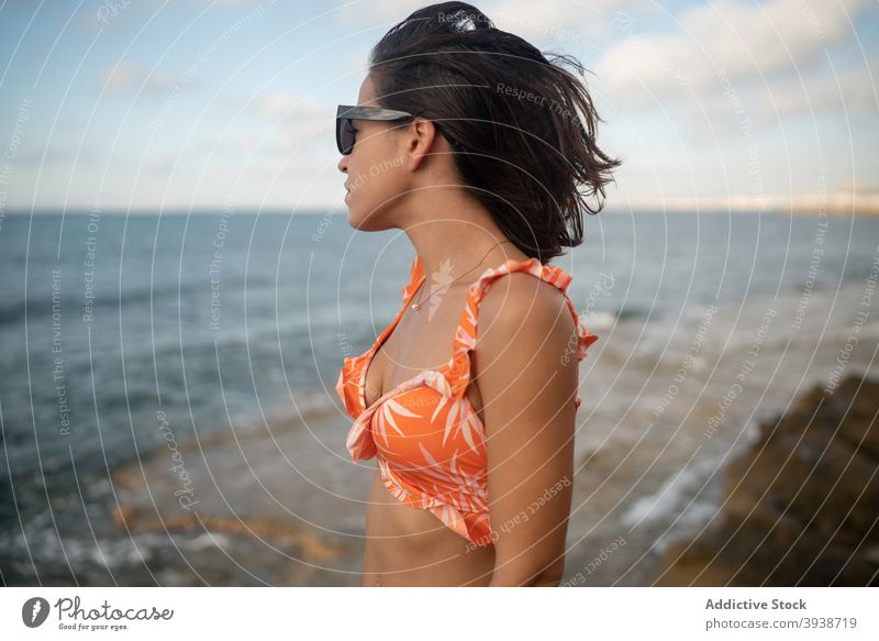 Pensive young ethnic woman relaxing on seacoast against cloudy sunset sky seashore vacation dreamy recreation nature traveler style holiday enjoy female