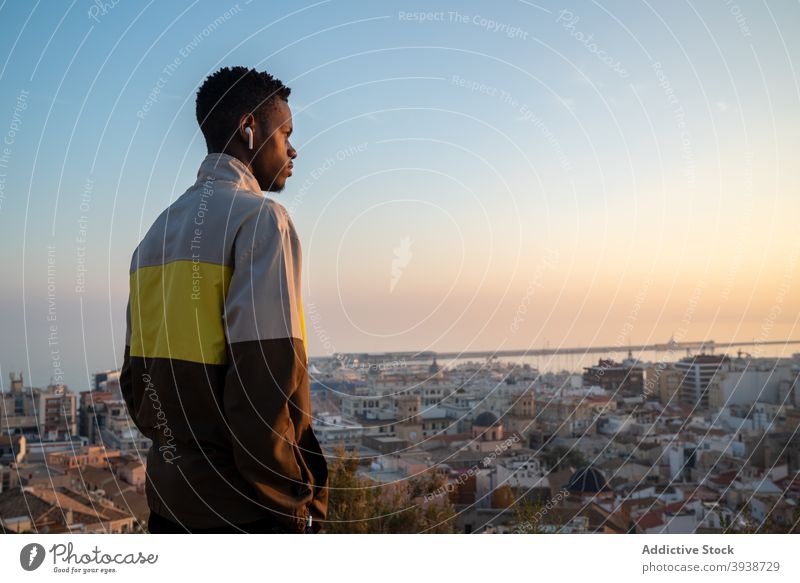 Thoughtful African American guy listening to music in TWS earphones and admiring cityscape man admire sea sunset confident thoughtful relax recreation