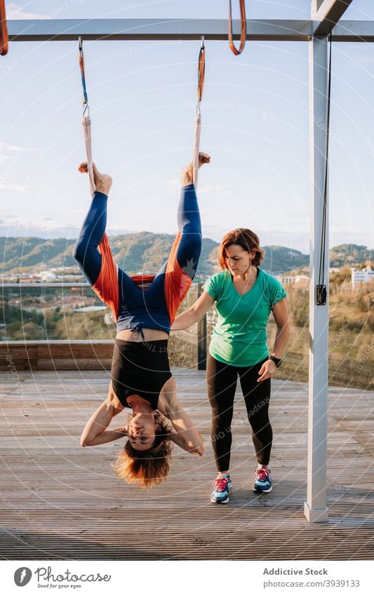 Woman doing yoga in hammock with support of instructor personal women practice hang asana flexible help female pose activewear terrace sunny together healthy