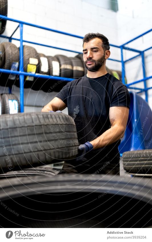 Man with tires in car workshop man mechanic service tyre technician busy male repairman various occupation serious workman maintenance confident handyman beard