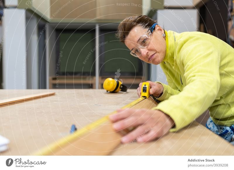 Focused young female joiner using measuring roulette in workshop woman measure woodwork concentrate joinery wooden plank carpenter professional job meter