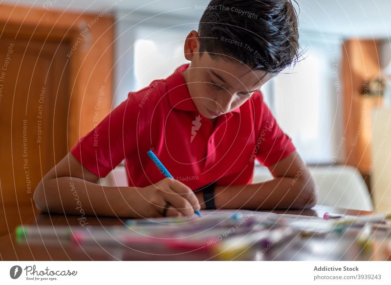 Schoolboy using marker while doing homework at table assignment write study draw knowledge copybook learn task education primary notebook colorful pen child