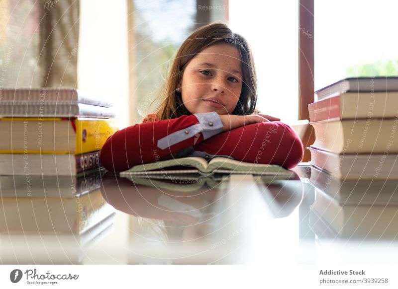 Adorable child reading book at table at home education learn homework assignment diligent textbook schoolgirl pupil bookworm kid pile knowledge literature