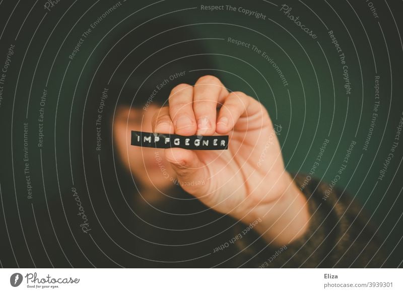 A woman holds a label with the word "anti-vaccination" on it into the camera. opponent Middle finger Immunization in solidarity corona Covidiot inoculate sb.