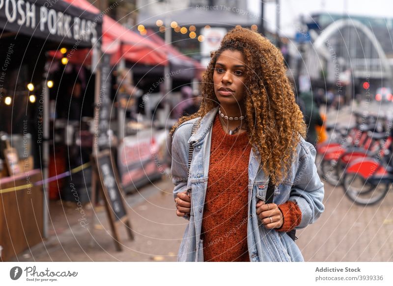 Stylish ethnic female teenager walking on street near market and looking away woman city pensive style traveler sightseeing souvenir trendy relax young black