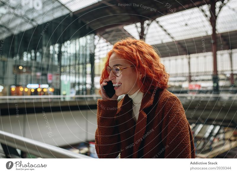 Cheerful woman talking on smartphone at railway station cheerful speak railroad redhead red hair female mobile conversation phone call communicate smile chat