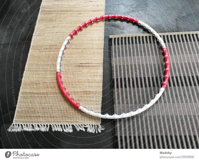 Hula hoops in red and white on two plain modern carpets made of natural fibre on the grey concrete floor of a designer apartment hula hoop Tire Fitness Sports