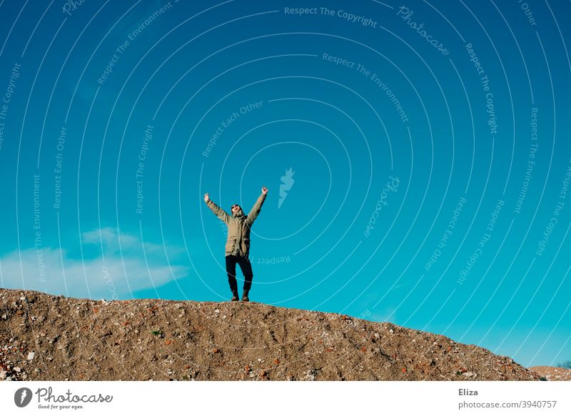 A man stands on a gravel hill against a blue sky and joyfully stretches his arms in the air Joy Freedom Blue sky Arms in the air pleased Good mood Hill Sky