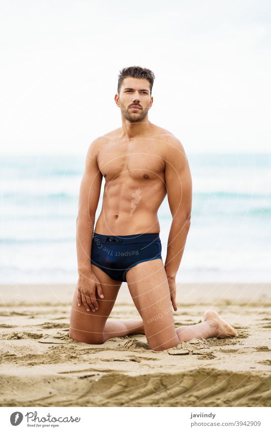 Handsome man on his knees on the sand of the beach sexy male muscular handsome healthy water people fit sea model abs vacation fitness chest strong attractive