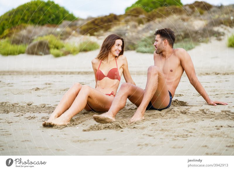 Young couple sitting together on the sand of the beach woman bikini summer body leisure lifestyle female girl coast outdoors enjoying people white swimwear fit