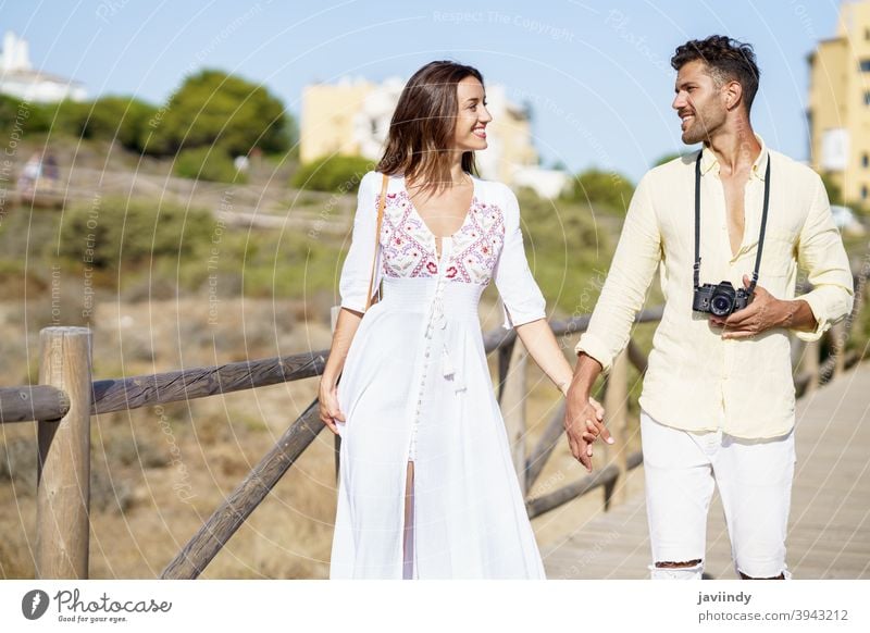 Loving couple walking along a wooden path towards the beach in a coastal area. vacation traveler tourist woman resort people holding hands love nature leisure